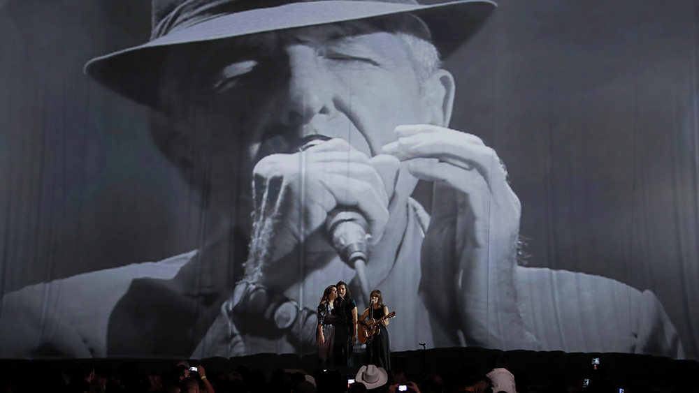 Feist on stage in front of a Leonard Cohen Photo